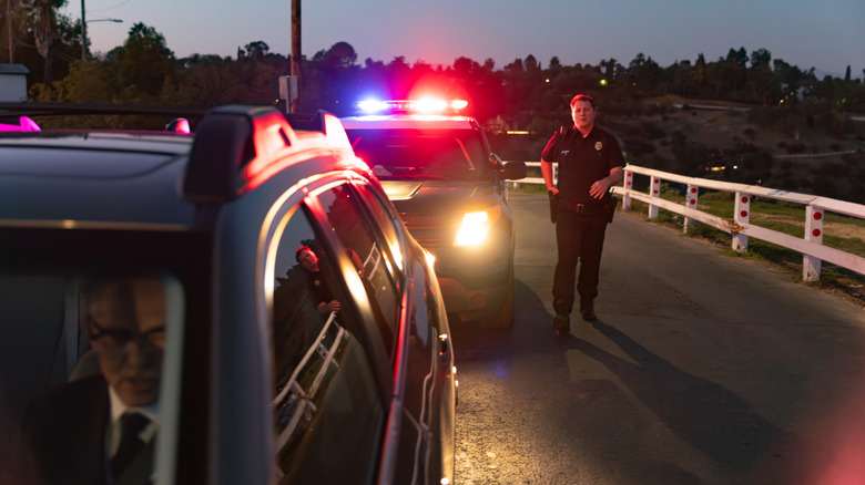 A police officer walks from his car to a senior driver in an SUV