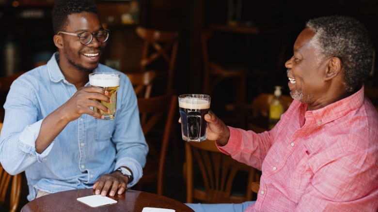 Younger and older Black men holding beer glasses