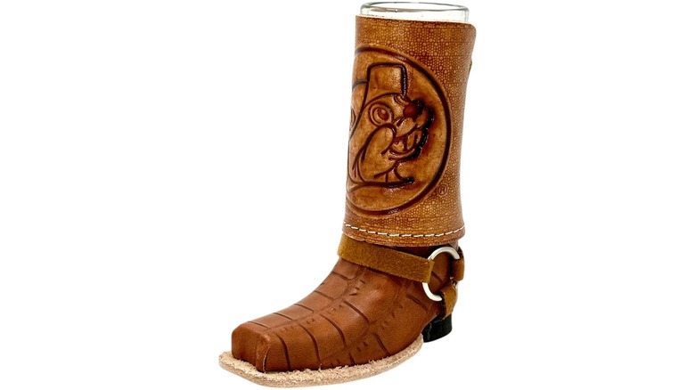 A mini brown leather cowboy boot with a shot glass inside against a white background