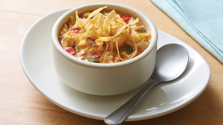 A white, plated cup of Applebee's Chicken Tortilla Soup on a table and with a spoon