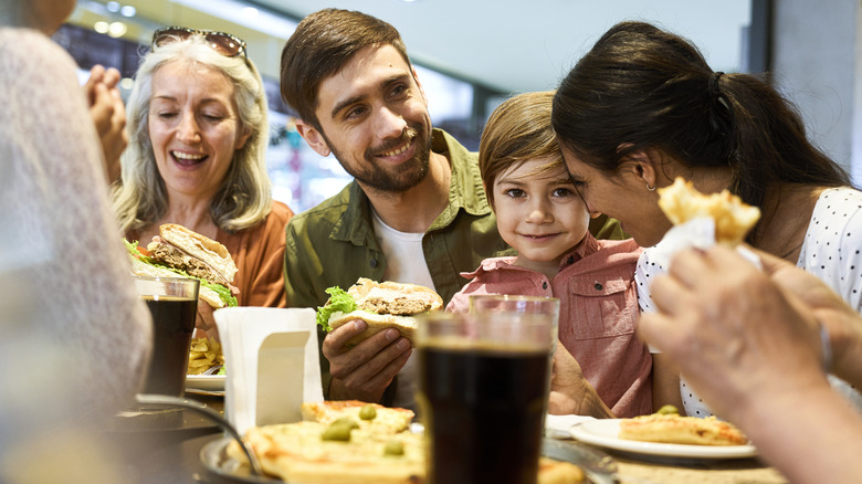 A group of people eat and laugh at a restaurant with lots of food on the table