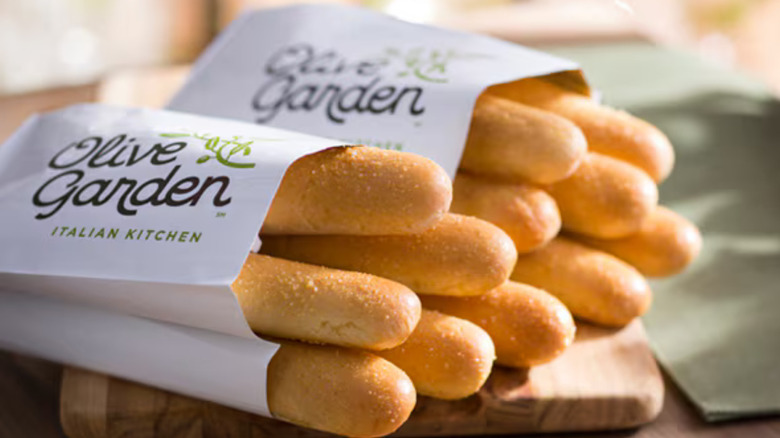 Two paper bags full of Olive Garden breadsticks on a wooden table