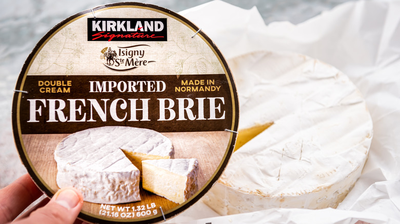A hand holding a wheel of Kirkland Signature Brie