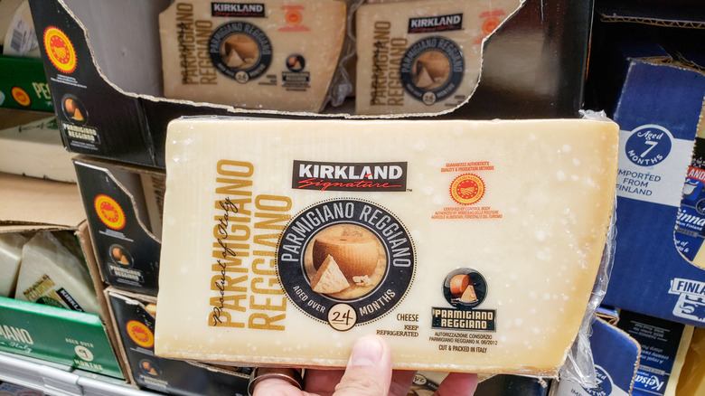 A hand holding Kirkland Signature Parmigiano Reggiano in front of store shelves