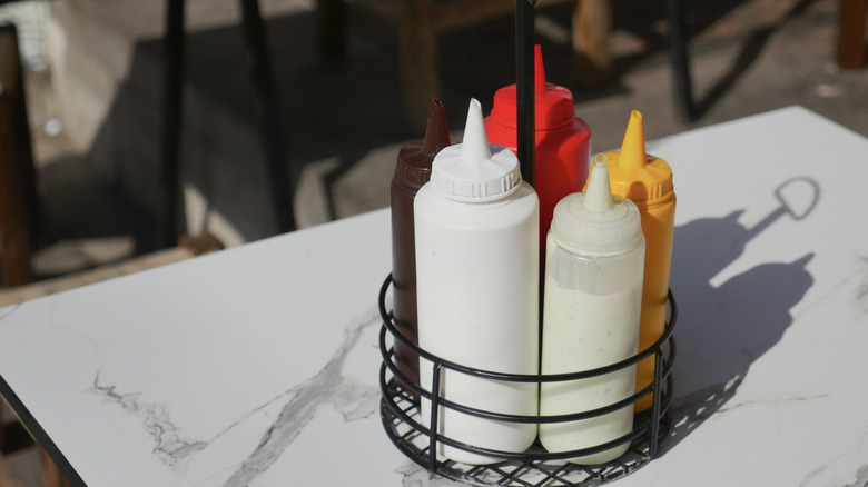 A condiment caddy with bottles of white sauce, mustard, and ketchup on a white restaurant table