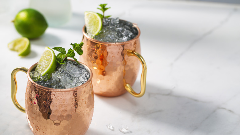Two Moscow mule copper mugs with lime and mint garnish on a white marble table