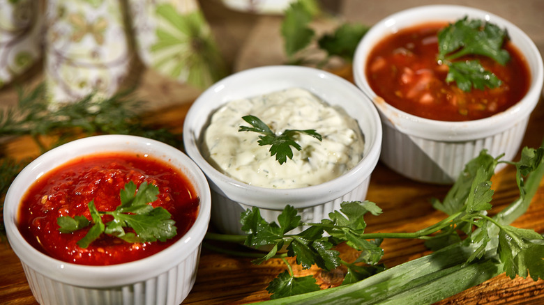 Three white ramekins filled with white or red sauce with a parsley garnish on top