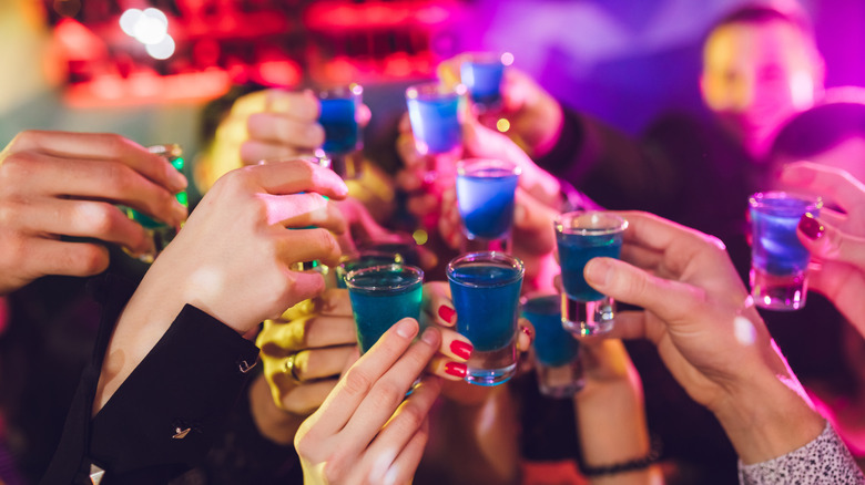 Several hands holding up blue shots in a cheers