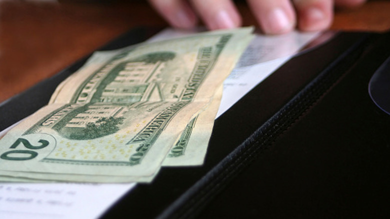 A close-up of a hand placing $20 bills on a black checkbook