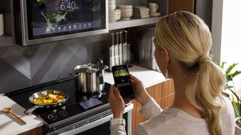 woman in kitchen operating her smart oven with her phone