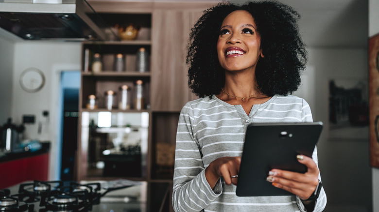 hand in kitchen holding phone with overlay images of smart home app icons