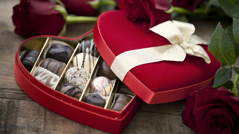Open heart-shaped box of chocolates with white ribbon.