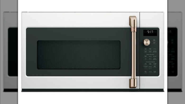 A large silver-colored over-the-range microwave oven, with a gold door handle and knob
