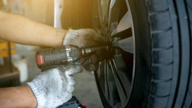 A mechanic using an impact gun on a tire installed on a car.