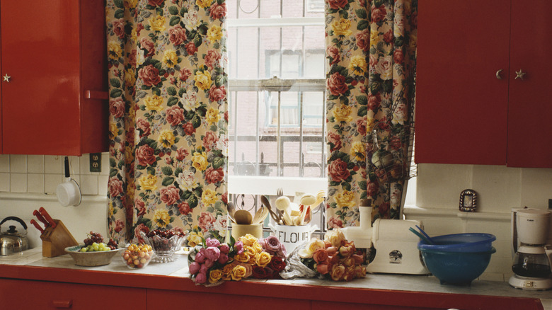 A vintage kitchen with reddish-brown cabinets and floral curtains