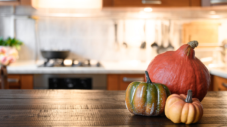 Three decorative gourds on a wood kitchen island with the stove and white counters and backsplash out of focus in the back.