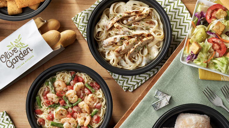 A photo of selection of Olive Garden to-go containers with pasta, salad, and breadsticks on a tablescape