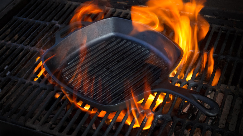 A cast iron skillet preheating over an open flame on a grill