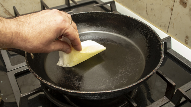 A hand wipes the bottom of a cast iron skillet to clean or oil it