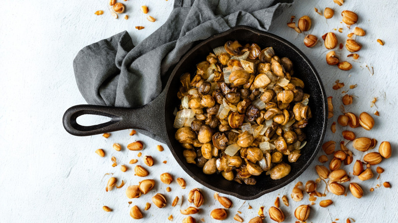 A cast iron skillet filled with corn kernels on a white background scattered with corn kernels