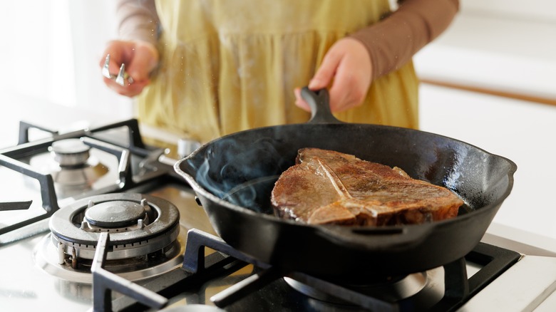 A person searing a steak on the stove using a cast iron skillet