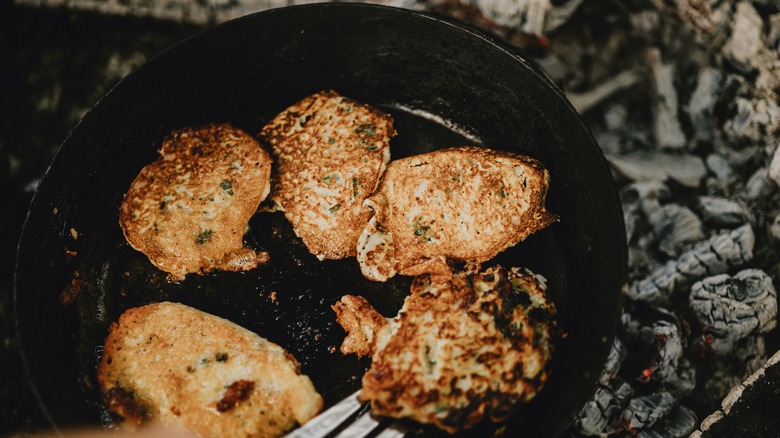 A cast iron skillet cooking potato pancakes over a campfire