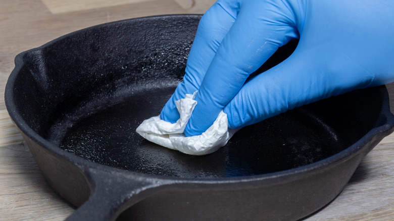Close up of a gloved hand seasoning a cast iron skillet
