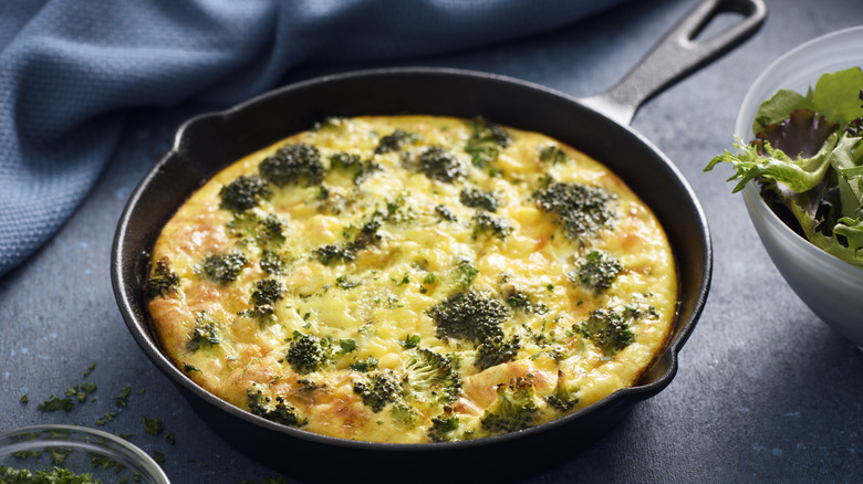 Homemade baked quiche in a cast iron pan against a blue cloth background