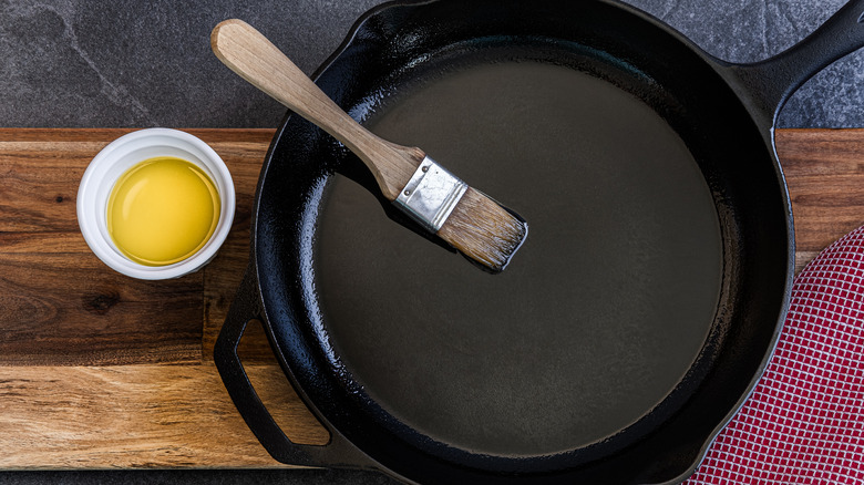 A cast iron pan with an oil brush next to a small bowl of oil