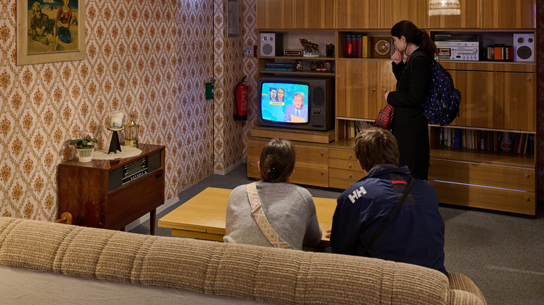 Three people watch television in '70s-style living room