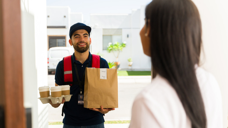 A delivery driver hands a brown bag and a coffee tray to a person outside a door