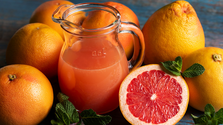 Pitcher of grapefruit juice surrounded by grapefruits and one cut in half