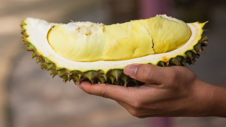 A hand holds a large chunk of durian fruit