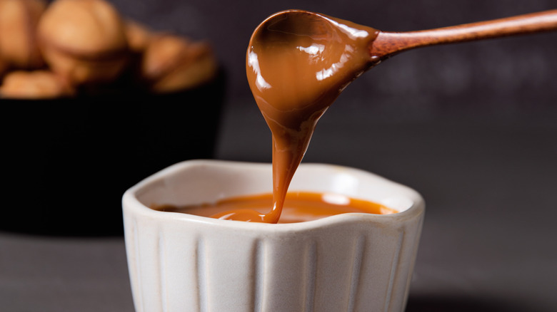 Spoon dipped in caramel sauce in a white bowl against a dark background