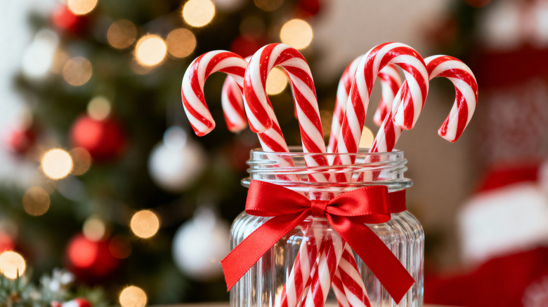 Candy canes in glass jar with an out-of-focus Christmas tree in the background