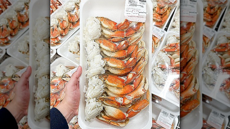 A hand holding a styrofoam container with crab claws and crab meat