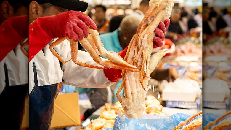 A server at the H Mart seafood counter holding up giant crab legs