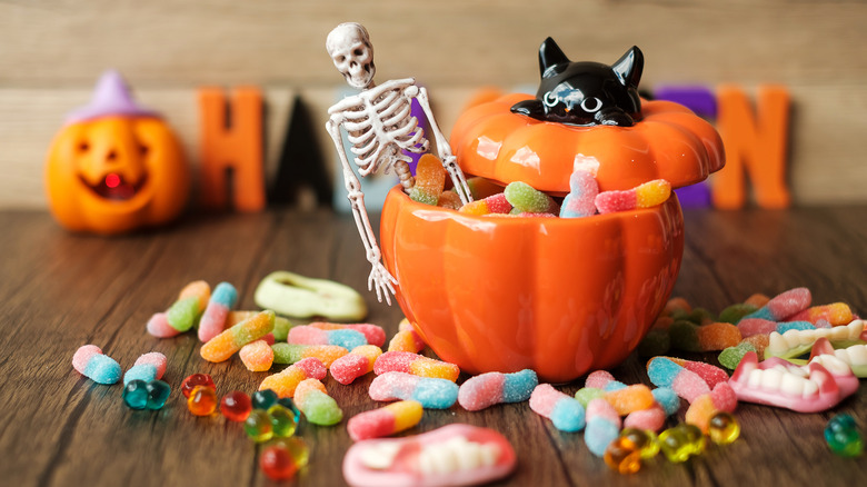 An assortment of gummy worms and rings inside and around a ceramic Halloween-themed pumpkin bowl