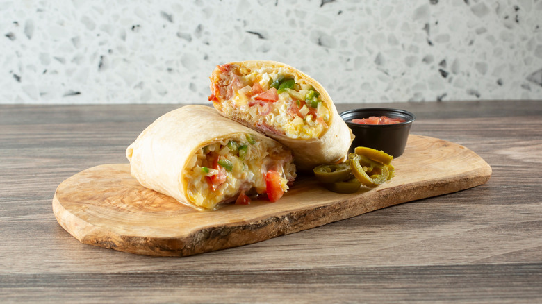 A breakfast burrito cut in half on a chopping board