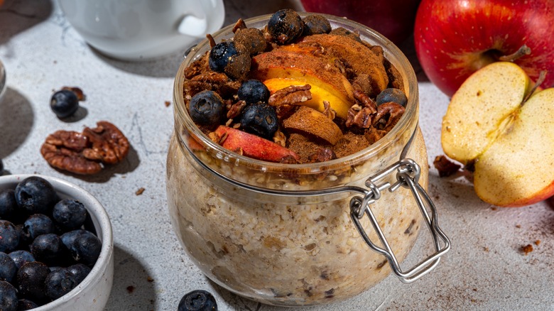 Overnight oats in a large clip-top jar, topped with fruit, nuts, and coco powder