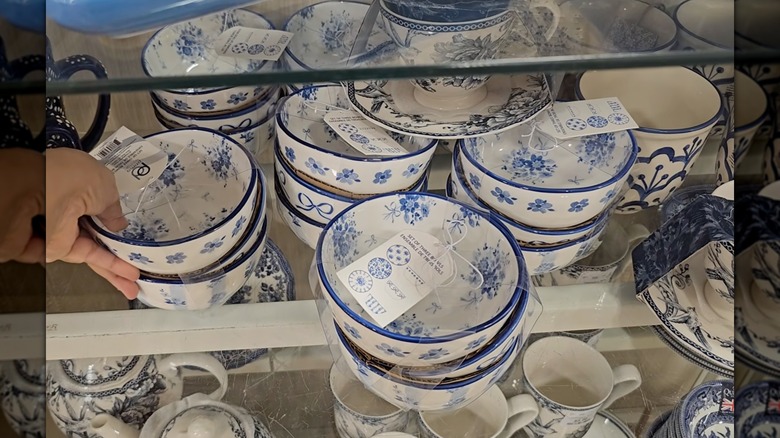 A hand touching a set of blue and white bowls, next to multiple other sets of blue and white bowls on a HomeGoods shelf