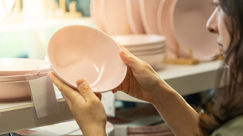 A woman holding a pink bowl in front of a display of dishes in a store