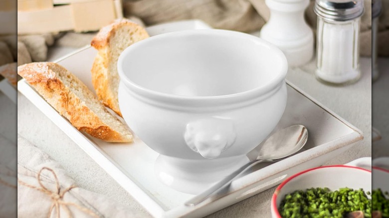 A white bowl with a lion head decoration on a white tray with two slices of bread