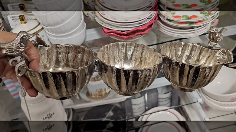 A hand holding a metal snack bowl with bird decoration at a HomeGoods store