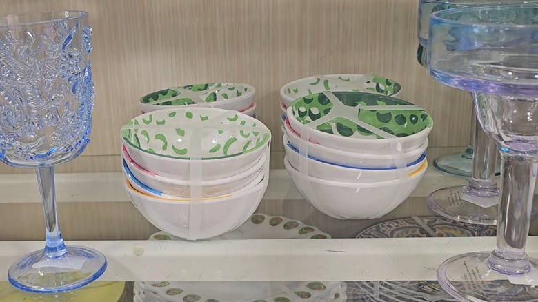 Four sets of four multicolored bowls on a HomeGoods shelf next to blue glasses