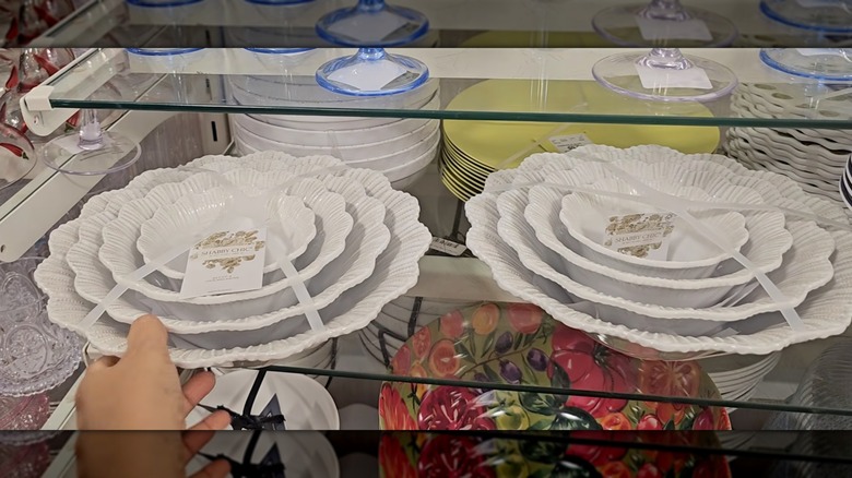 A hand touching a set of four white bowls with scalloped edges on a HomeGoods shelf