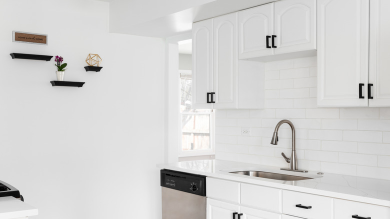 A brgiht white domestic kitchen, with ornaments arranged on the back wall