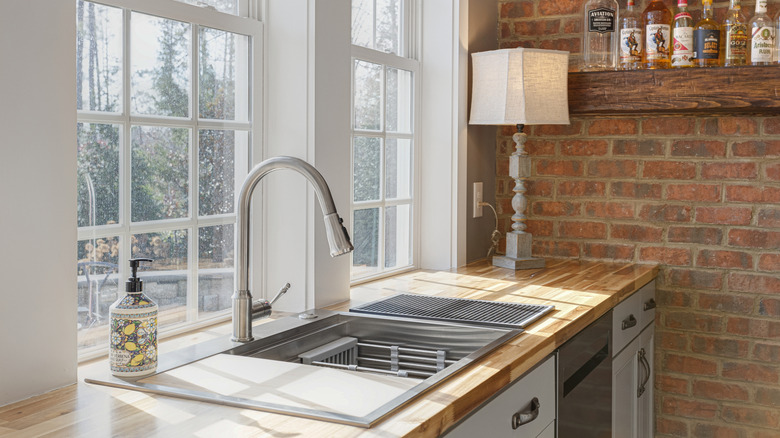 A farmhouse-style kitchen, showing the sink, a rustic lamp, and a shelf of liquor bottles