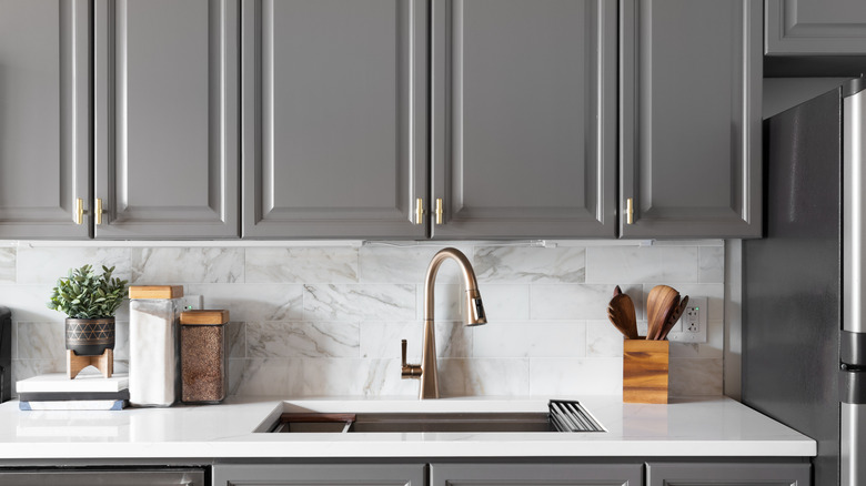 A kitchen with gray cabinets and a gray backsplash