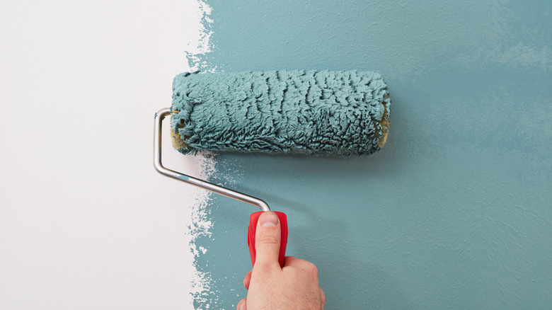 A hand rolls blue paint onto a surface